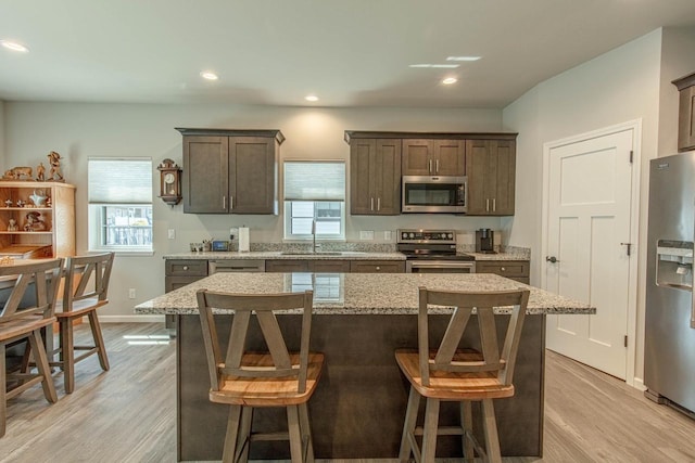 kitchen with appliances with stainless steel finishes, sink, light stone countertops, and a center island