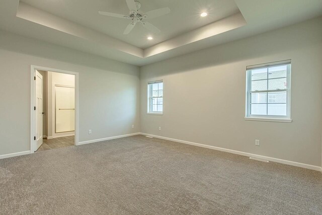 unfurnished room with light carpet, ceiling fan, and a raised ceiling