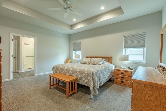 carpeted bedroom featuring ceiling fan, a raised ceiling, and ensuite bath