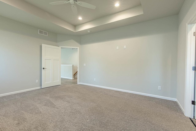 spare room with a tray ceiling, light colored carpet, and ceiling fan