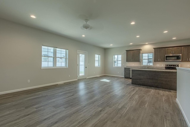 kitchen with sink, light stone counters, stainless steel appliances, dark wood-type flooring, and dark brown cabinets