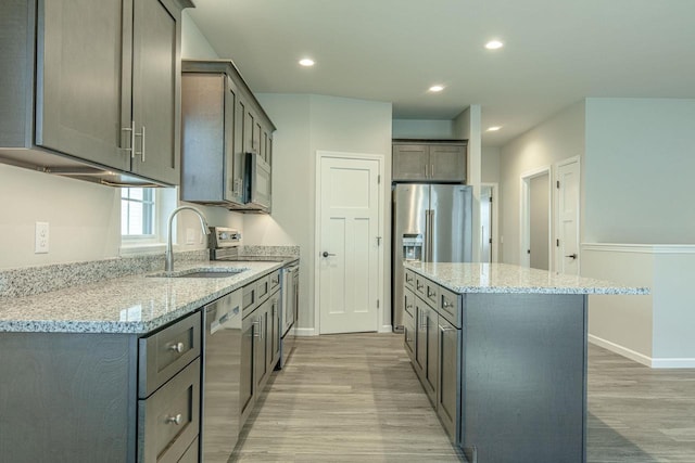 kitchen with sink, appliances with stainless steel finishes, a center island, and light stone counters