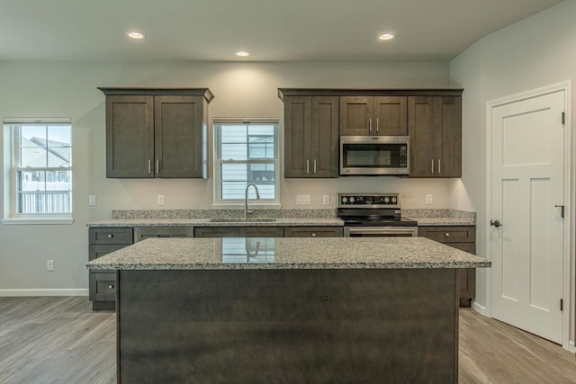 kitchen with a center island, appliances with stainless steel finishes, light stone countertops, and dark brown cabinets