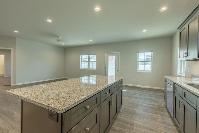 kitchen featuring a kitchen island, dishwasher, light stone countertops, and light hardwood / wood-style floors