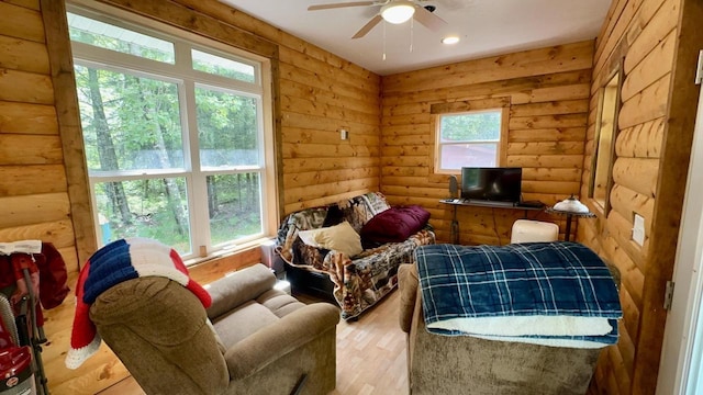 sitting room with ceiling fan, wood-type flooring, and log walls