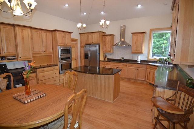 kitchen featuring an inviting chandelier, light wood-type flooring, wall chimney exhaust hood, a kitchen island, and stainless steel appliances