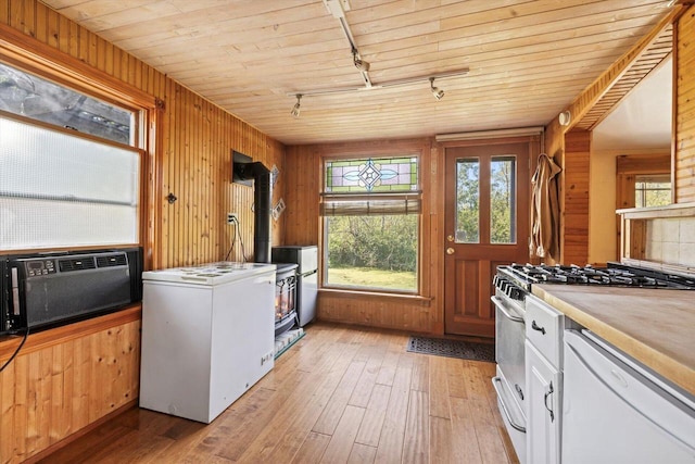 kitchen with light hardwood / wood-style flooring, a wood stove, wood walls, white cabinets, and white appliances