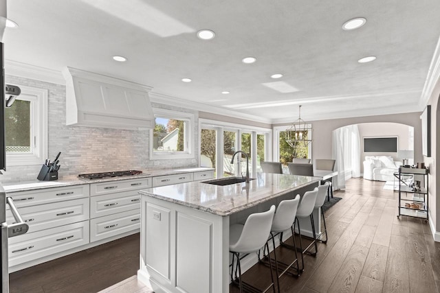 kitchen with dark wood-type flooring, an island with sink, white cabinets, premium range hood, and sink