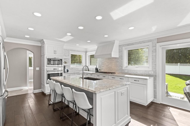 kitchen with white cabinetry, an island with sink, light stone counters, dark hardwood / wood-style flooring, and custom exhaust hood