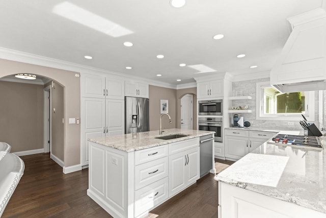 kitchen featuring appliances with stainless steel finishes, white cabinetry, dark wood-type flooring, light stone counters, and a center island with sink