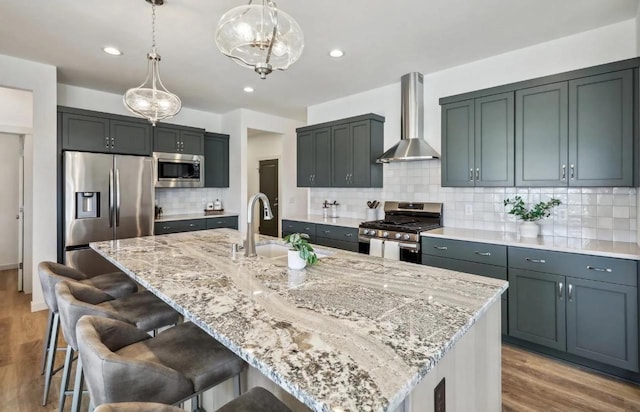 kitchen featuring a center island with sink, appliances with stainless steel finishes, wall chimney exhaust hood, and pendant lighting