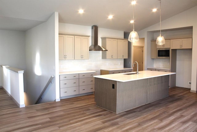 kitchen featuring an island with sink, dark hardwood / wood-style flooring, sink, wall chimney range hood, and pendant lighting