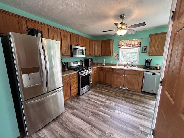 kitchen featuring ceiling fan, wood-type flooring, sink, a textured ceiling, and stainless steel appliances