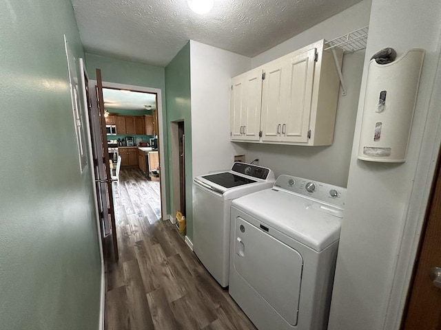 clothes washing area with washing machine and dryer, a textured ceiling, dark hardwood / wood-style flooring, and cabinets