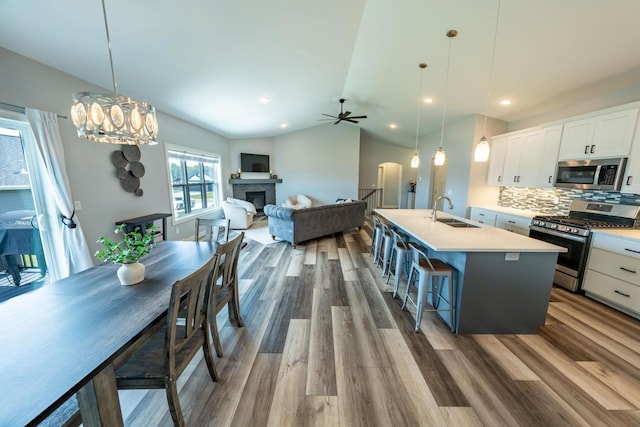 kitchen with appliances with stainless steel finishes, decorative light fixtures, white cabinetry, and a kitchen island with sink