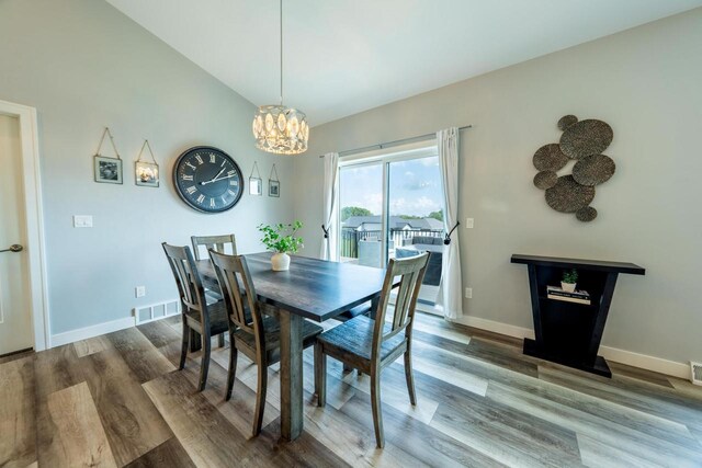 dining room featuring hardwood / wood-style floors, vaulted ceiling, and a chandelier