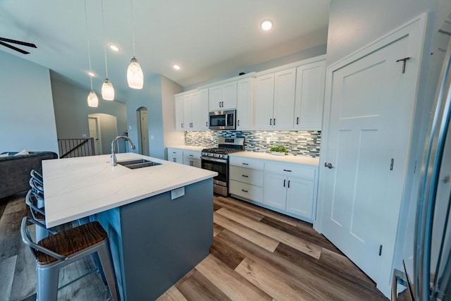 kitchen with sink, appliances with stainless steel finishes, white cabinets, and a kitchen island with sink