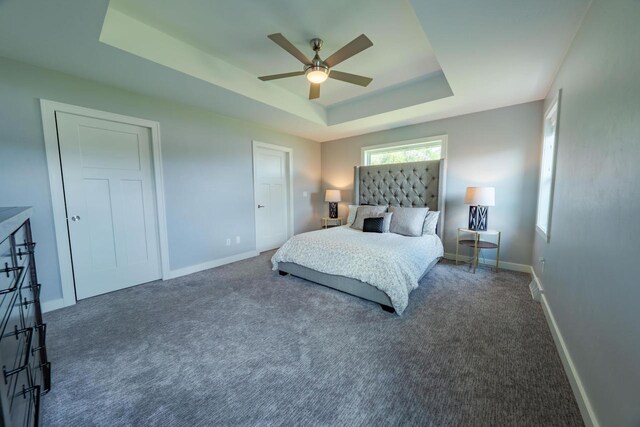 bedroom with dark carpet, ceiling fan, and a tray ceiling