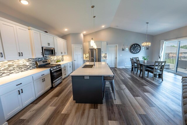 kitchen with decorative light fixtures, stainless steel appliances, a kitchen island with sink, and white cabinets