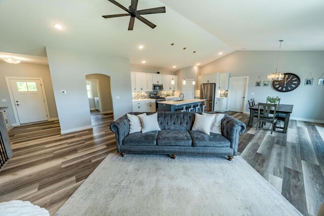 living room featuring ceiling fan with notable chandelier, sink, dark wood-type flooring, and lofted ceiling