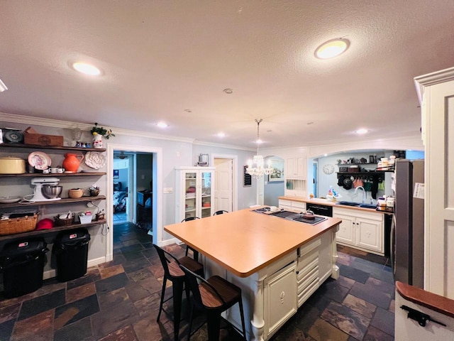 kitchen with decorative light fixtures, crown molding, a center island, sink, and white cabinetry