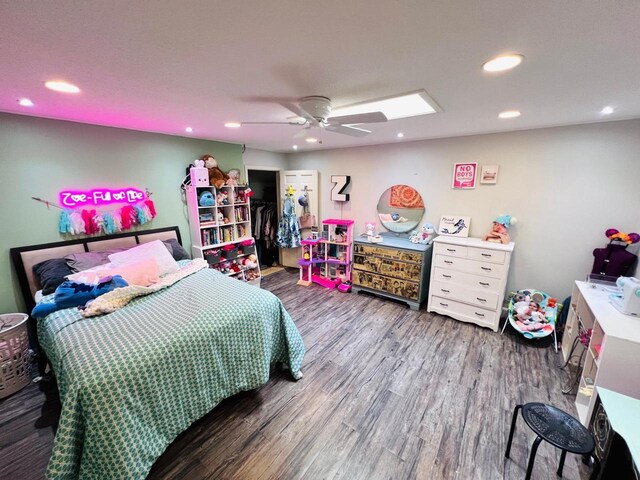 bedroom featuring a walk in closet, a closet, ceiling fan, a skylight, and hardwood / wood-style floors