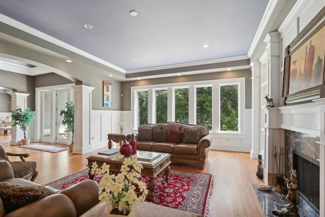 living room featuring a high end fireplace, hardwood / wood-style floors, crown molding, and ornate columns