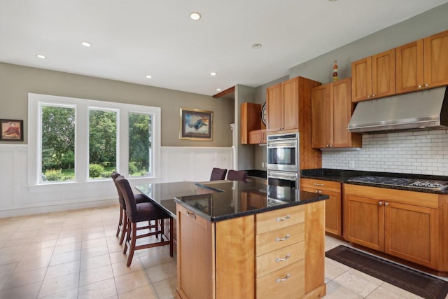 kitchen with gas stovetop, tasteful backsplash, double oven, a center island, and light tile patterned flooring