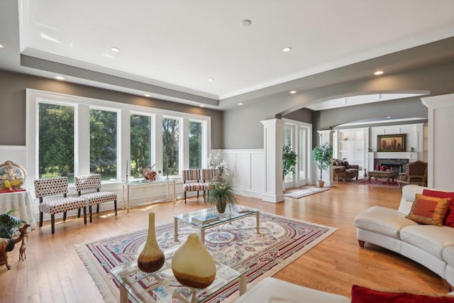 living room with light wood-type flooring, a raised ceiling, and ornate columns