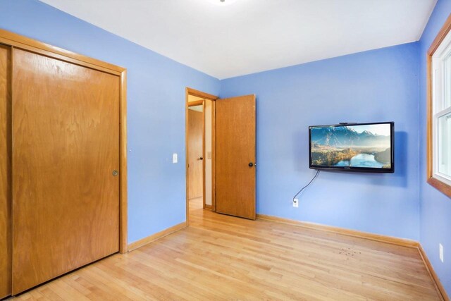 unfurnished bedroom with light wood-type flooring, a closet, and multiple windows