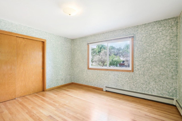 unfurnished bedroom featuring wood-type flooring, a baseboard radiator, and a closet