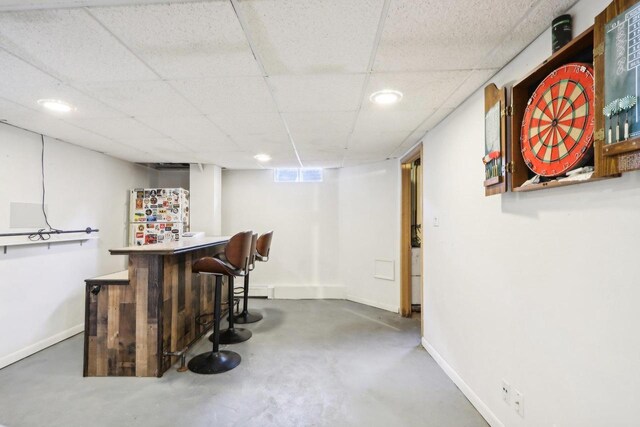 bar featuring a paneled ceiling, concrete flooring, and white fridge