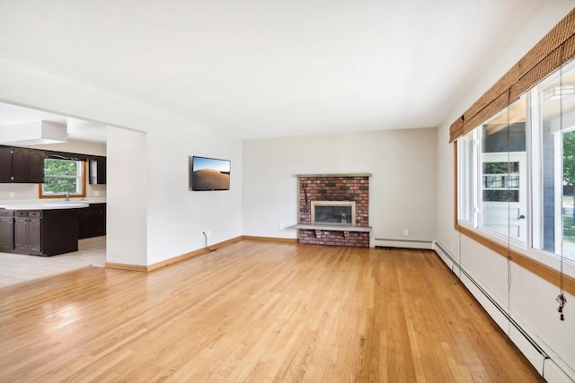 unfurnished living room featuring sink, light hardwood / wood-style flooring, a brick fireplace, and a baseboard radiator