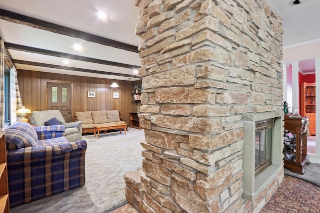 carpeted living room featuring a fireplace, beamed ceiling, crown molding, and wood walls