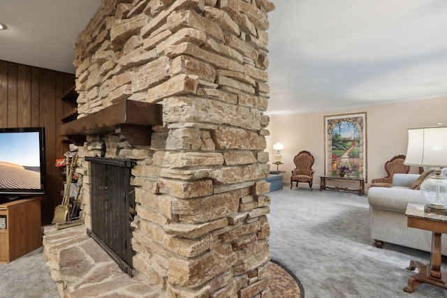 carpeted living room with ornamental molding, wood walls, and a stone fireplace