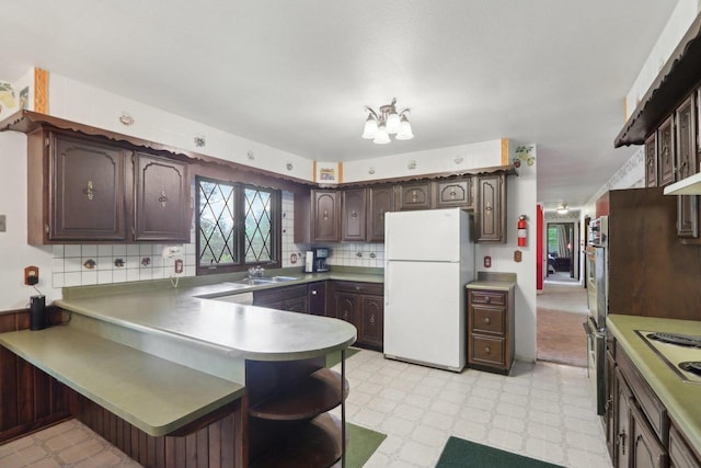 kitchen with kitchen peninsula, dark brown cabinetry, sink, white appliances, and decorative backsplash