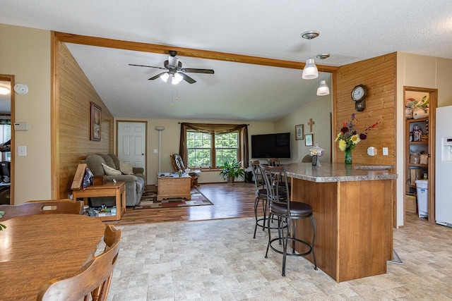 kitchen featuring ceiling fan, light hardwood / wood-style flooring, wood walls, vaulted ceiling, and a textured ceiling