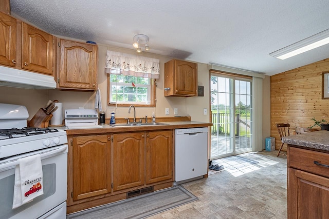 kitchen featuring sink, white appliances, vaulted ceiling, a textured ceiling, and wooden walls