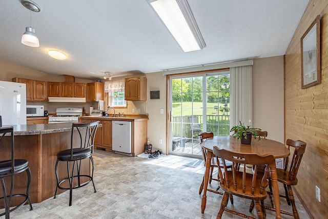 kitchen with wooden walls, a breakfast bar area, decorative light fixtures, and white appliances