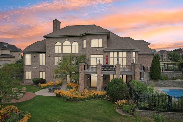 back house at dusk with a patio, a balcony, and a lawn