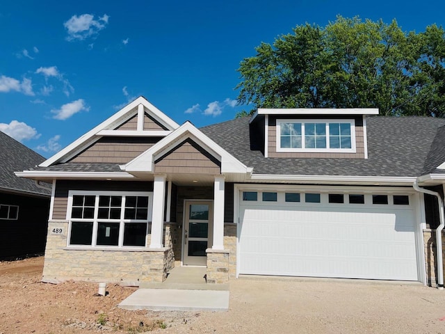 view of front of house with roof with shingles, driveway, and stone siding