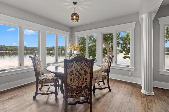 dining space featuring a water view, ornate columns, and hardwood / wood-style floors