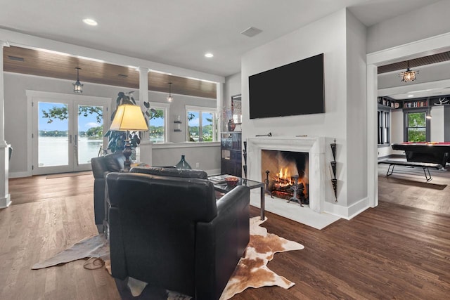 living room with a water view, a high end fireplace, french doors, and hardwood / wood-style floors