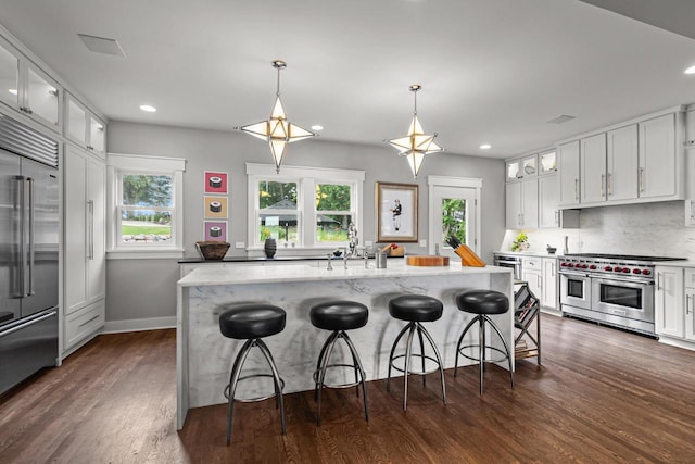 kitchen with a breakfast bar, high quality appliances, hanging light fixtures, white cabinets, and an island with sink