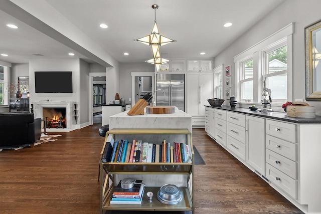 kitchen with hanging light fixtures, white cabinets, dark hardwood / wood-style floors, built in fridge, and a kitchen island with sink