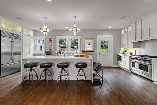 kitchen with a center island with sink, decorative light fixtures, high end appliances, white cabinets, and a kitchen breakfast bar