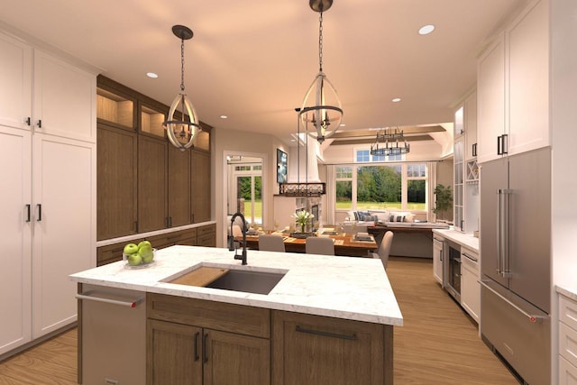 kitchen featuring white cabinetry, a kitchen island with sink, hanging light fixtures, sink, and built in refrigerator