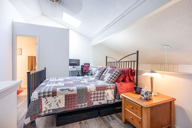 bedroom with vaulted ceiling with skylight, a textured ceiling, and light wood-type flooring