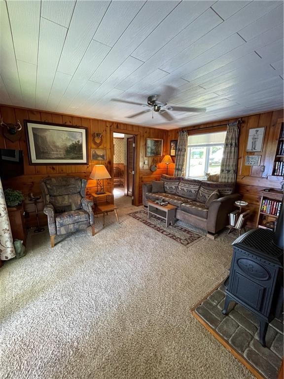 living room with wood walls, ceiling fan, carpet, and a wood stove