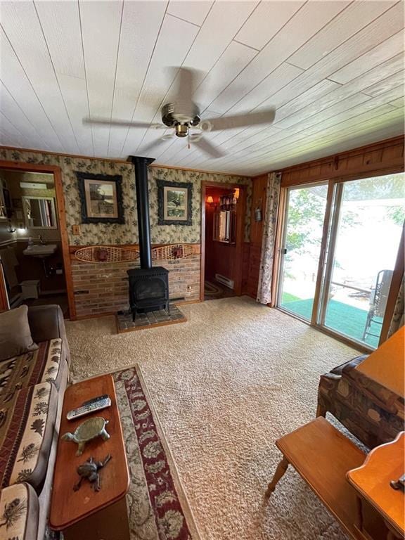 living room with ceiling fan, a wood stove, wood walls, wooden ceiling, and carpet flooring